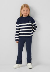 Maglione a righe blu navy con strisce bianche, presenta un fiocco decorativo, abbinato a leggings blu navy e sneaker bianche, texture liscia.
