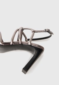 Metallisk silver högklackad sandal med tre remmar, en justerbar ankelspänne och en fyrkantig klack. Texturerat fotbädd, elegant design.