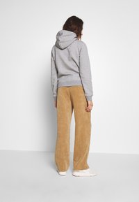 Sudadera gris con capucha y puños acanalados, combinada con pantalones de pana anchos de color beige. El calzado son zapatillas blancas. Fondo simple.