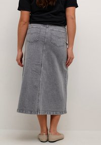 Siva denim maksi krilo z rahlo A-linijo, zadnjimi žepi in vertikalno šivno podrobnostjo, ki teče po sredini. Oblečeno z črnim topom.