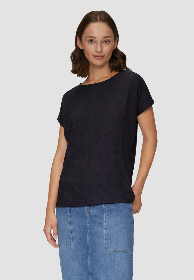 Czarny krótki top z luźnym krojem, z teksturowanym wzorem i okrągłym dekoltem, w połączeniu z niebieską spódnicą dżinsową.