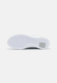 Semelle de chaussure blanche avec des rainures horizontales et un petit carré gris comportant un logo Puma près du talon sur un fond uni.