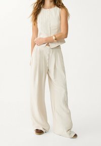 Two-piece outfit in light beige fabric; sleeveless buttoned top paired with wide-leg, high-waisted pants. Simple and textured.