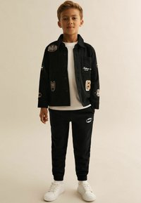 Must värvitud särk, millel on plaastrid; valge T-särk all; mustad dressipõlved Batmani logoga; valged spordijalatsid; casual, keha sulandav stiil.