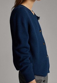 Granatowy, prążkowany kardigan z okrągłym dekoltem, pięcioma guzikami i długimi rękawami. Miękka tekstura i dopasowany krój.