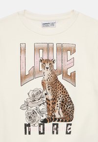 Φούτερ σε κρεμ απόχρωση με γραφικό λεοπάρδαλη και το κείμενο "ΑΓΑΠΑ ΠΕΡΙΣΣΟΤΕΡΟ," διακοσμημένο με ασημένια καρφίτσες και εικονογραφήσεις τριαντάφυλλων.