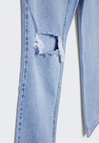 Vaqueros de denim azul claro con una rodilla desgastada y bordes deshilachados, diseño de pierna recta y estilo clásico de cinco bolsillos.