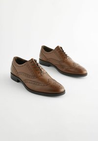 Chaussures habillées en cuir marron avec des détails en brogue, finition lisse, bout arrondi et semelle noire. Fermeture à lacets à six œillets.
