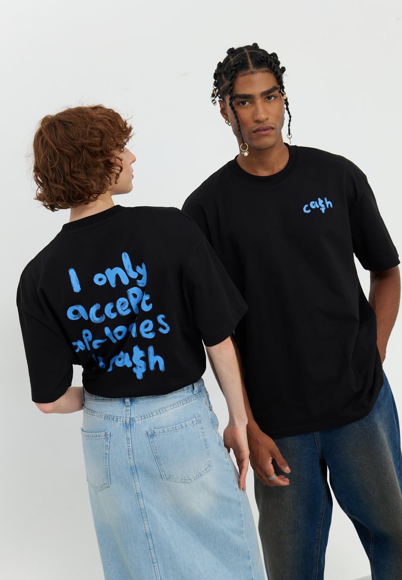 Juodos didelės t-shirt'os su ryškiu mėlynu tekstu; vienoje marškinėlių užrašas "Aš priimu tik kalorijas ir šiukšles," o kituose - "grynaisiais."