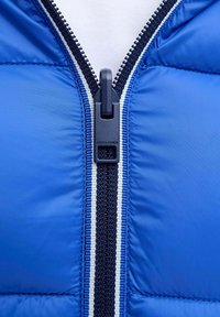 Nahaufnahme eines blauen gesteppte Jackenreißverschlusses mit schwarzem Zipperzug und weiß gestreiftem dunkelblauem Reißverschlussband.