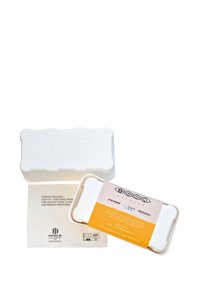 Bílý pouzdro na brýle s zaoblenými hranami, s embosovaným logem a žlutou etiketou. Obsahuje kompostovatelný sáček uvnitř. Jednoduchý, čistý design.