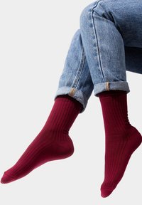 Burgundowe skarpetki z prążkowanym wzorem o miękkiej fakturze, ściśle dopasowane w kostce, w zestawie z podwiniętymi jasnoniebieskimi dżinsami.