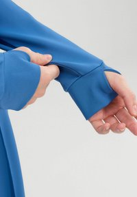 Prenda de manga larga azul con tejido suave y elástico. Presenta un orificio para el pulgar en el puño y un diseño ajustado para mayor comodidad y flexibilidad.