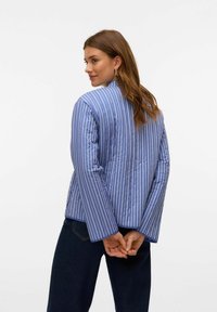 Giacca a vento blu a righe con design trapuntato e maniche larghe, caratterizzata da righe bianche verticali e scollo rotondo.