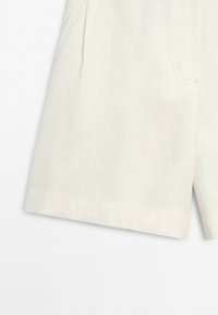 Close-up of the bottom half of off-white linen shorts with a pocket and subtle seam details on a light background.