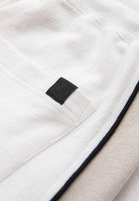 Hvid sweatshirtstof med en tekstureret overflade, der har et lille sort mærke og kontrasterende navy kant langs kanten.
