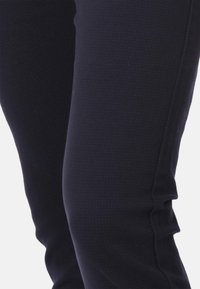 Pantaloni blu scuro con una texture liscia e un motivo sottile, caratterizzati da una vestibilità slim e senza dettagli hardware visibili.