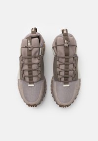 Ett par taupe och beige träningsskor med dragflikar, elastiskt snörsystem och robusta sulor sett uppifrån på vit bakgrund.