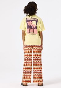 T-shirt jaune avec un graphique de palmier au dos ; associé à un pantalon large avec un motif zigzag multicolore.