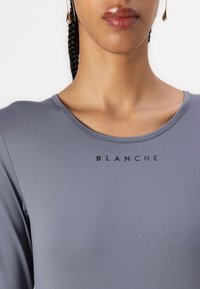 Gray long-sleeve top featuring a scoop neckline and the word "BLANCHE" printed in black across the chest; smooth, stretch fabric texture.