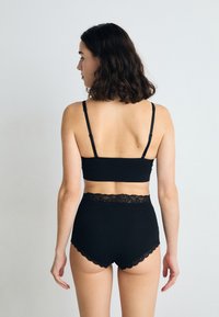 Black cotton bralette with thin straps paired with high-waisted black panties. Panties feature a scalloped lace waistband detail.