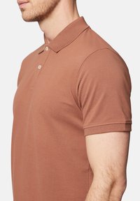 Brązowa koszulka polo z żebrowanym kołnierzykiem, trzyguzikowym zapięciem, krótkimi rękawami i teksturowanym wzorem materiału.