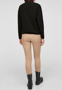 Zwarte gebreide sweater met een casual pasvorm, gecombineerd met strakke beige broek en zwarte enkellaarzen met een zijrits.