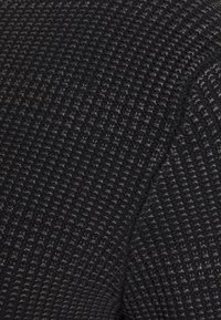 Czarna dzianina o fakturowanym wzorze, z siatkowym designem. Materiał wydaje się miękki i przytulny, z subtelnymi różnicami w odcieniach.