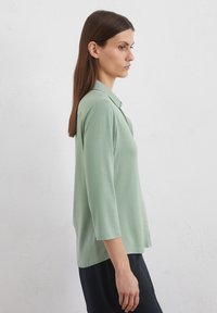 Light green, collared blouse with three-quarter sleeves and a relaxed fit. Smooth texture; hem falls just below the hips.