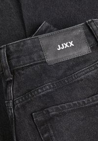 Svart denimjeans med en läderetikett som har "JJXX" i vitt. Tyget har en slät yta med sömmar och framfickor.