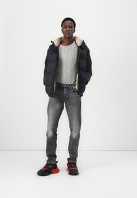 Black puffer jacket with beige lining, gray ribbed sweater, faded gray jeans, and black sneakers with red accents. Simple design, no patterns.