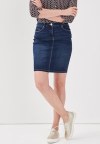 Jupe crayon en denim bleu foncé, dotée de poches avant et d'un design ajusté. Assortie à des baskets claires avec des détails perforés.
