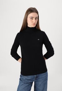 Pulover negru cu guler mediu, realizat dintr-un material moale, având mâneci lungi și un design ajustat. Detaliu mic cu logo pe piept.