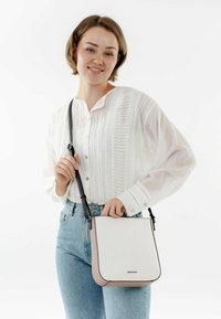 Bolso de cuero sintético blanco con acentos rosas, de forma plana y correa negra ajustable, sostenido por una persona que lleva una camisa blanca texturizada y jeans.