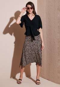 Zwarte wikkeltop met korte mouwen, gecombineerd met een asymmetrische rok met luipaardprint. Strappy zwarte sandalen maken de outfit af.