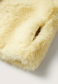 Miękki, puszysty, jasnokremowy materiał z małym otworem kieszeniowym, ukazujący różnice w strukturze oraz gęste, pluszowe włókna.