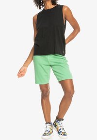 Haut sans manches noir, short vert clair et baskets à motifs vifs. Tissu lisse, coupe décontractée, short de longueur mi-cuisse.