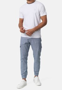 Weißes Baumwoll-T-Shirt mit navyfarbener Kragenapplikation, kombiniert mit hellblauen Cargo-Hosen mit elastischen Bündchen und weißen Sneakers. Lässige Passform und sichtbare Textur.