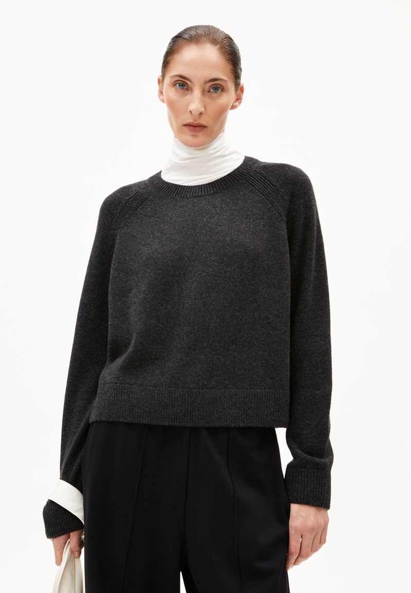 Pull en tricot gris foncé avec un col rond, des poignets et un ourlet côtelés. Associé à un col roulé blanc en dessous, offrant une coupe décontractée.