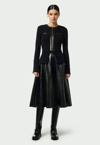 Svart tvådelad outfit bestående av en figursydd texturerad jacka med två dragkedjefickor och en utsvängd lädjerock. Slim-fit svarta stövlar fulländar looken.