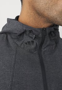 Černá texturovaná bunda s vysokým límcem a nastavitelnou kapucí, s předním zipem a decentním logem na hrudi.