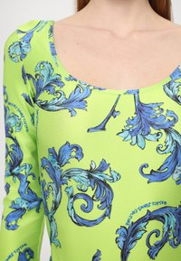 Grønn langermet bodysuit med scoop-hals, som har intrikate blå barokk mønstre og en glatt, elastisk stoffkvalitet.