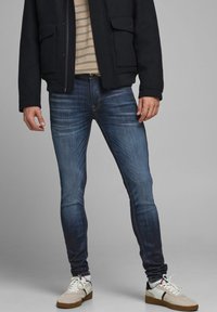Mörkblå skinny jeans med blekningsdetaljer, ihopparat med en beige och marinblå randig skjorta och en svart jacka. Skorna inkluderar vita sneakers.