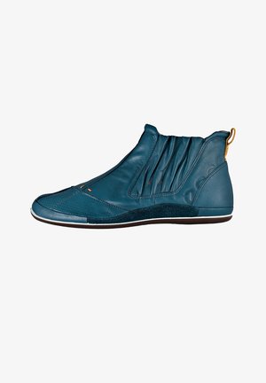Botas de tobillo de cuero verde azulado con parte superior plisada, costuras marcadas, puntera perforada y acento negro texturizado a lo largo de la suela. Tirador dorado en el talón.