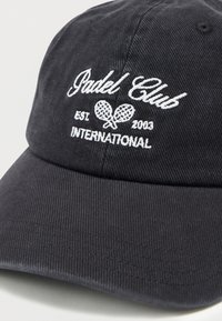 Μαύρο καπέλο μπέιζμπολ με λευκή κεντημένη επιγραφή "Pudel Club INTERNATIONAL EST. 2003" και λογότυπο με δύο σταυρωτές ρακέτες padel.