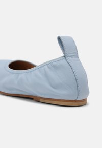 Ballerine plate en cuir bleu clair avec une languette au talon et une semelle plate beige, vue de côté et de dos.