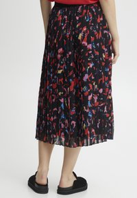 Zwarte plisse midi-rok met een abstract patroon dat rode, roze en blauwe tinten bevat. Elastische tailleband en een vloeiende stoftextuur.