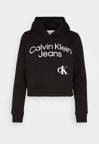 Sudadera negra recortada hecha de tela con una textura suave. Presenta texto blanco "Calvin Klein Jeans" y un pequeño logo "ck" en el frente.