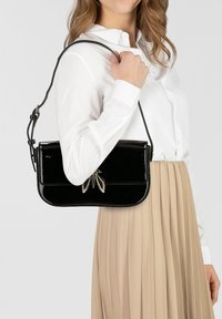 Zwarte handtas van lakleer met een gestructureerde vorm en een zilveren strikdetail. Hij heeft een lange verstelbare band en een glanzende afwerking.