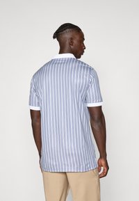 A polo shirt de manga curta apresenta riscas verticais azuis e brancas, um colarinho branco e uma textura de tecido suave.